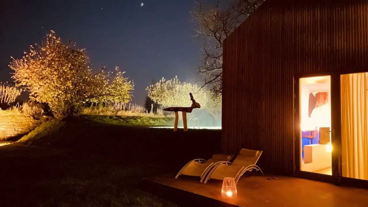 Het houten huis 's avonds met verlichte tuindeur, een lantaarn en verlichte fruitbomen onder de sterren