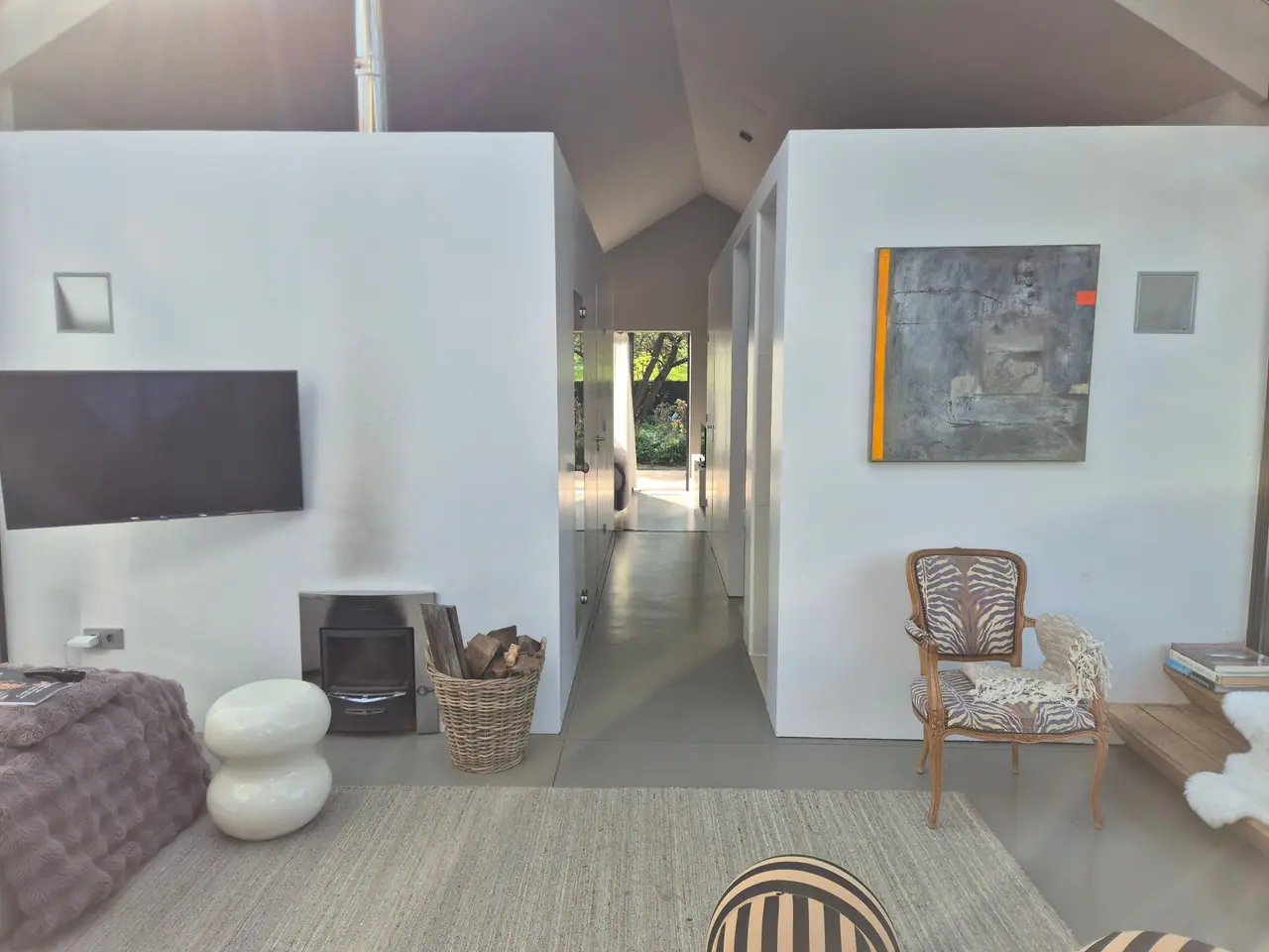 Witte volumes met houtkachel en kunst, met de gang naar de slaapkamer ertussen